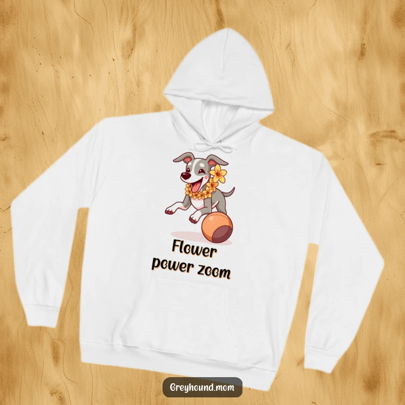 Funny Greyhound wearing a flower lei, joyfully running towards a rolling ball, soft and humorous hoodie.